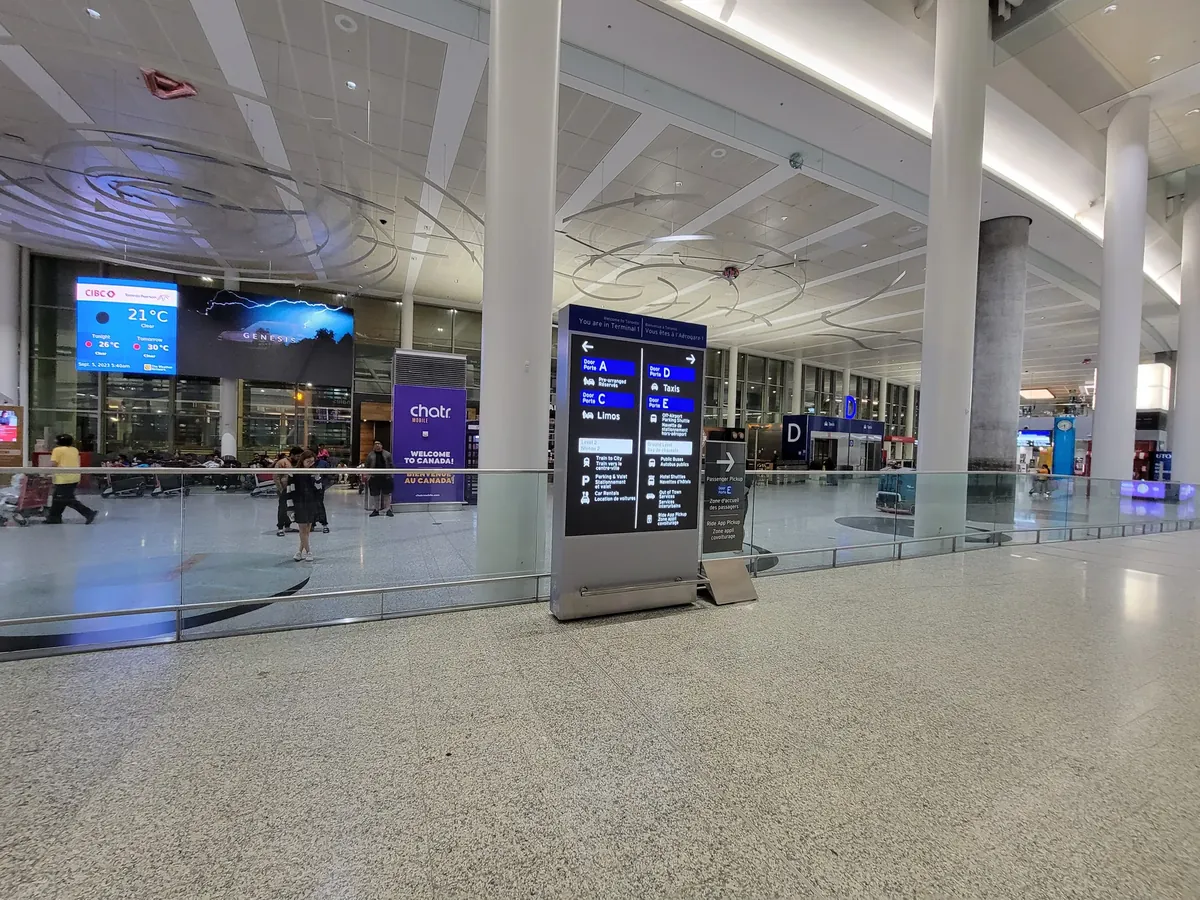 Travellers with luggage carts in the Terminal 1 arrivals hall at Toronto Pearson Airport, with a Limos pickup sign